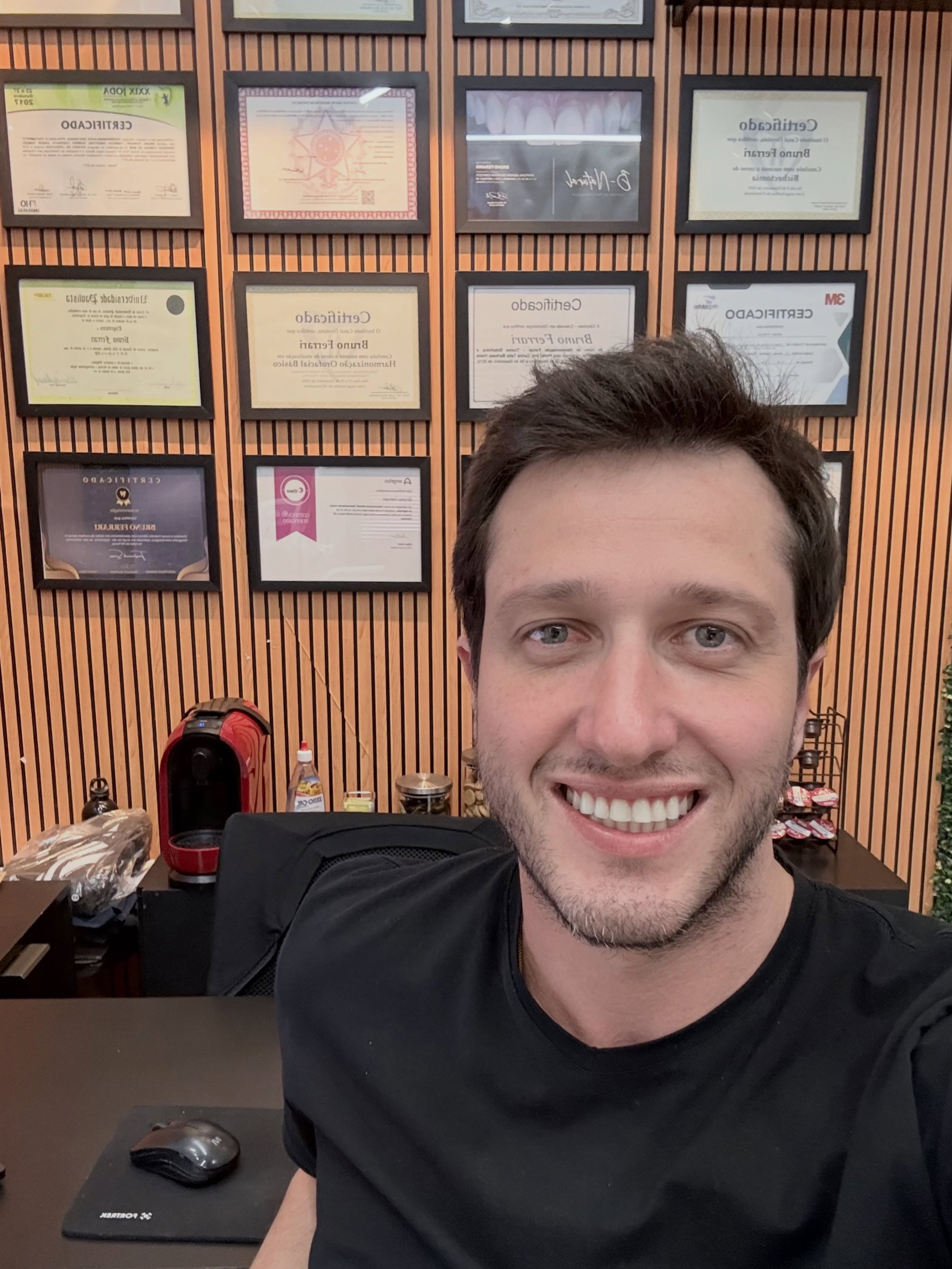 Dr. Bruno Ferrari na sala dele, com os certificados na parede de ripas de madeira